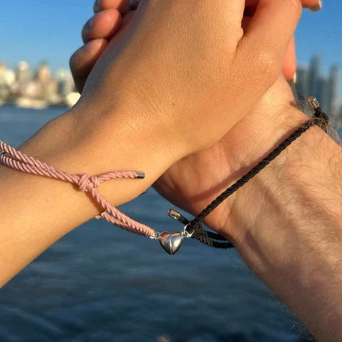 Couple holding hands wearing matching magnetic heart bracelets by the sea